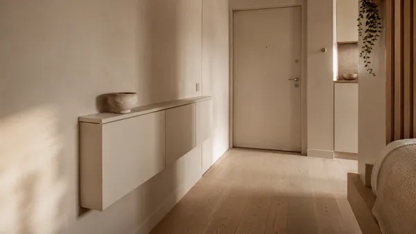 Tiny apartment entryway organization featuring a color-drenched slim floating shoe cabinet, light oak floors, and warm minimal decor.